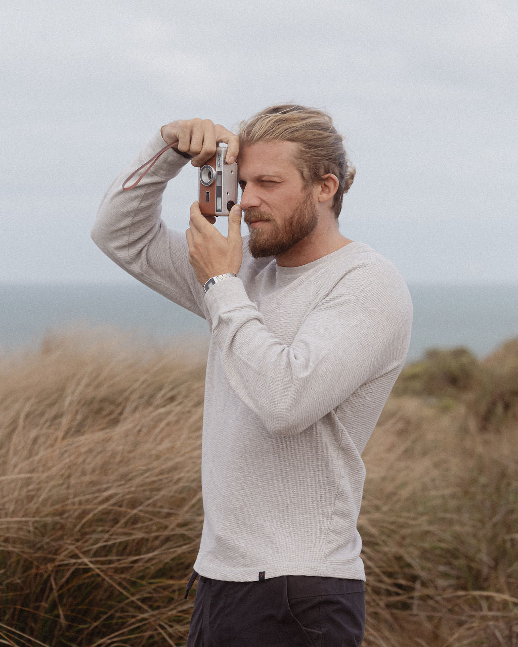 Man standing on coastal headland looking through a vintage Surfolk 35mm film camera, capturing the ocean view.