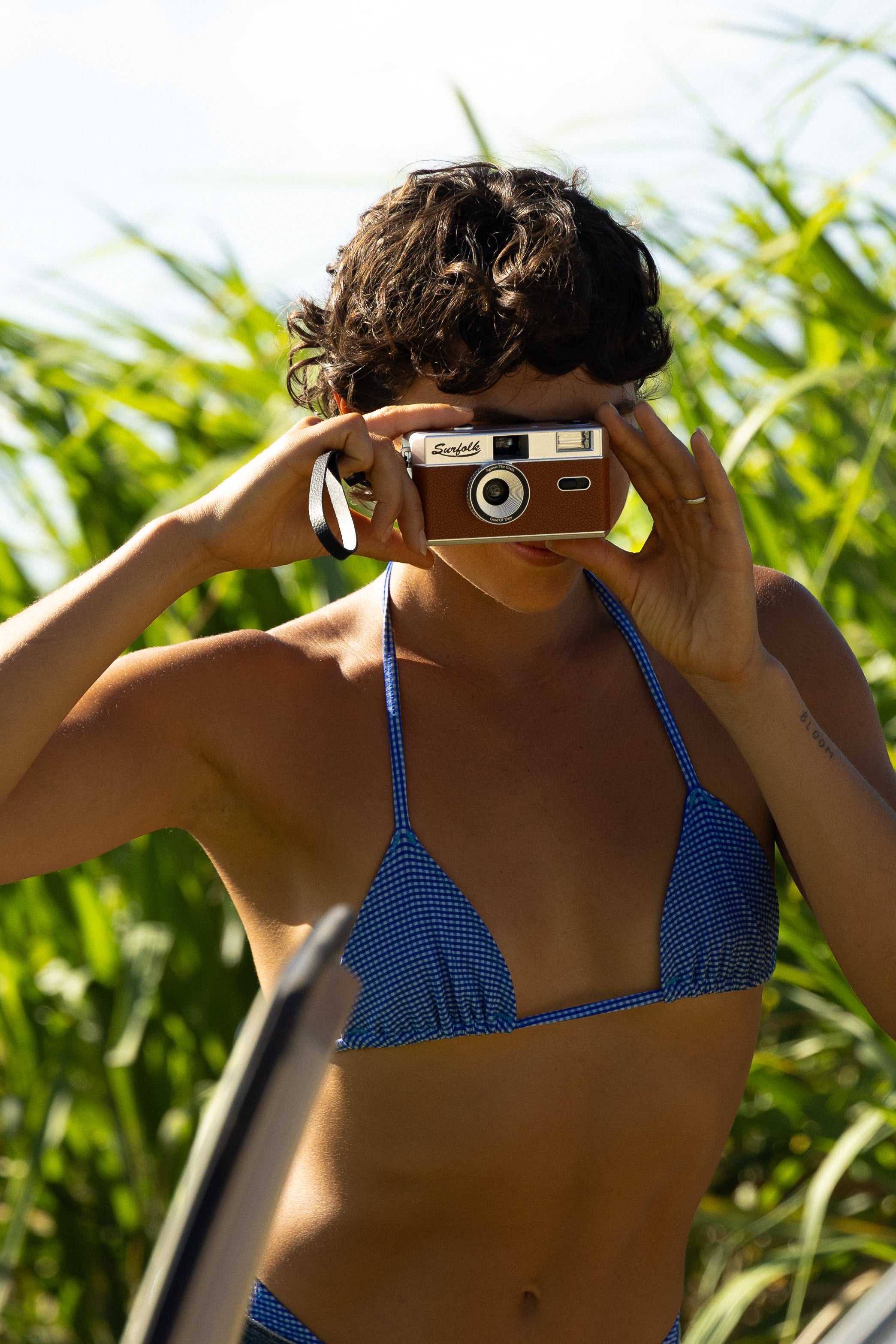 Person in a blue bikini holding a vintage camera with greenery in the background