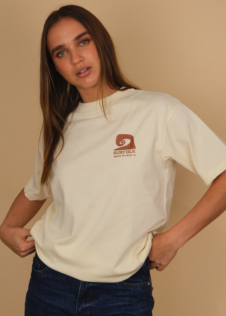 A woman modeling a cream-colored t-shirt with a brown &