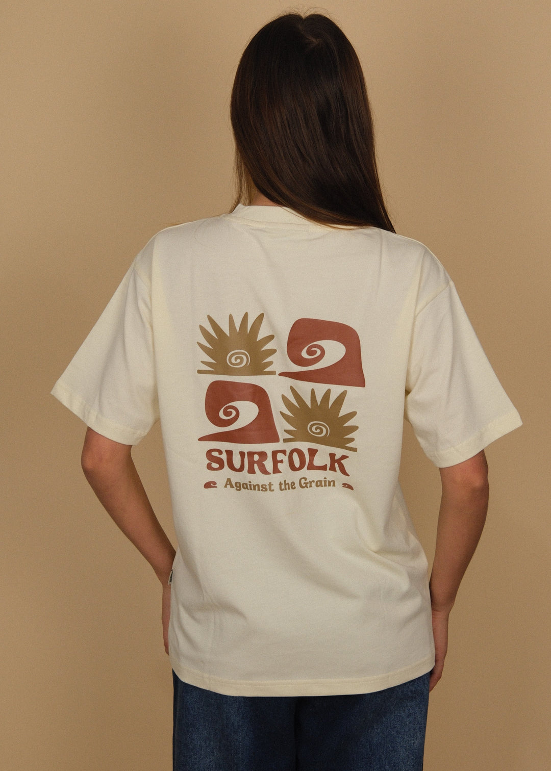 A woman viewed from behind wearing a cream-colored t-shirt with a brown and gold graphic on the back that reads &