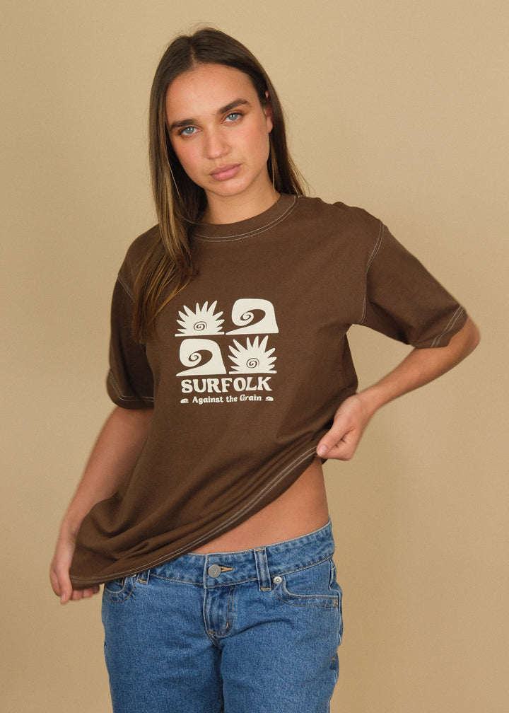 A woman modeling a brown short-sleeve t-shirt with a white graphic print that reads &