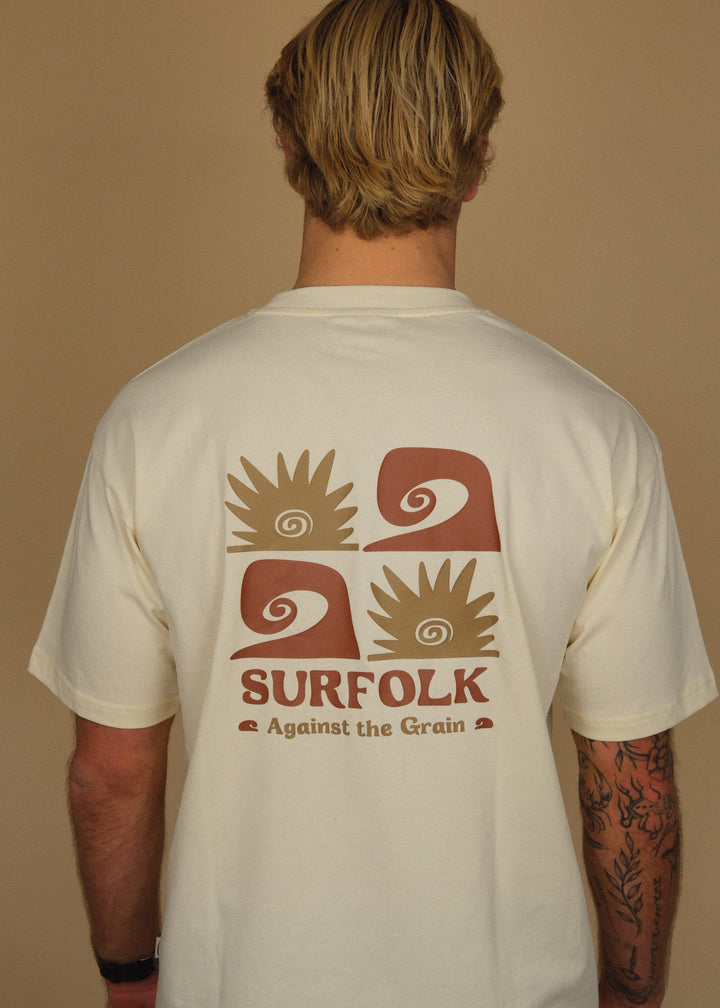 A man viewed from behind wearing a cream-colored t-shirt with a large brown graphic on the back that reads &
