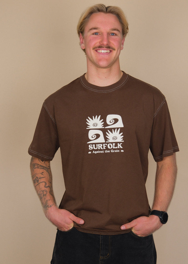 A smiling man with blonde hair and a mustache wearing a brown t-shirt with a white graphic print that says &