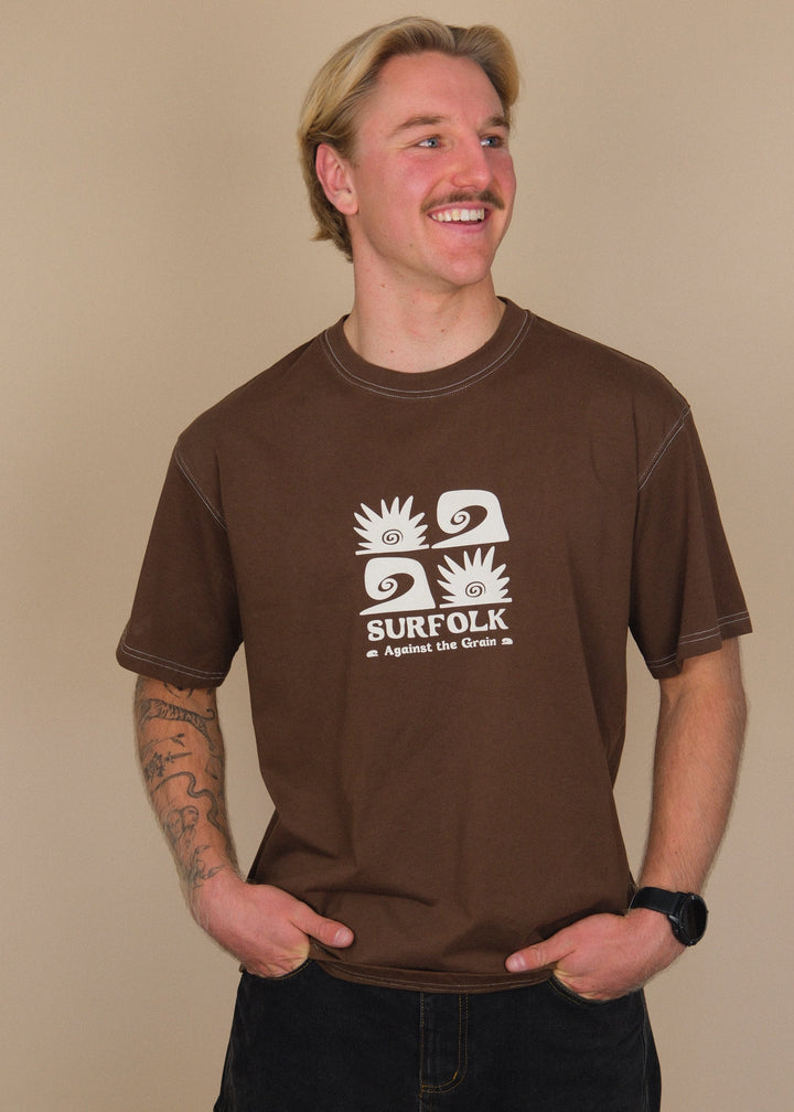 A smiling man with blonde hair and a mustache wearing a brown t-shirt with a white graphic that says &