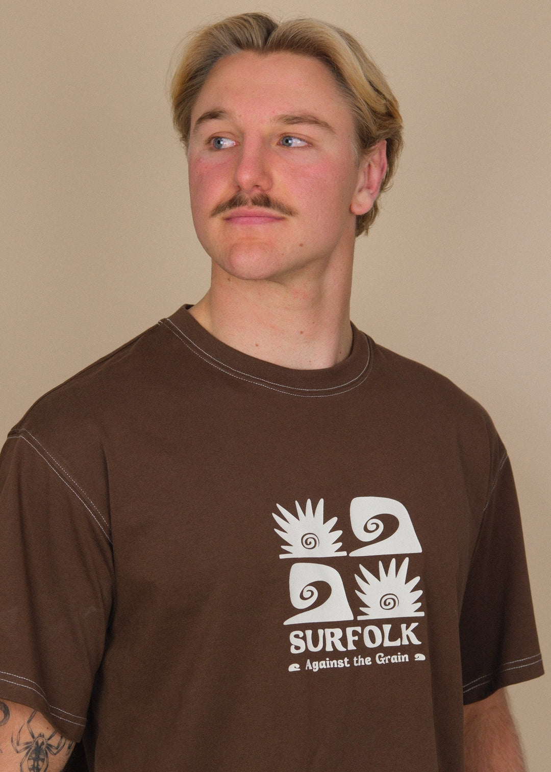 A man wearing a brown t-shirt with a white graphic print that reads &