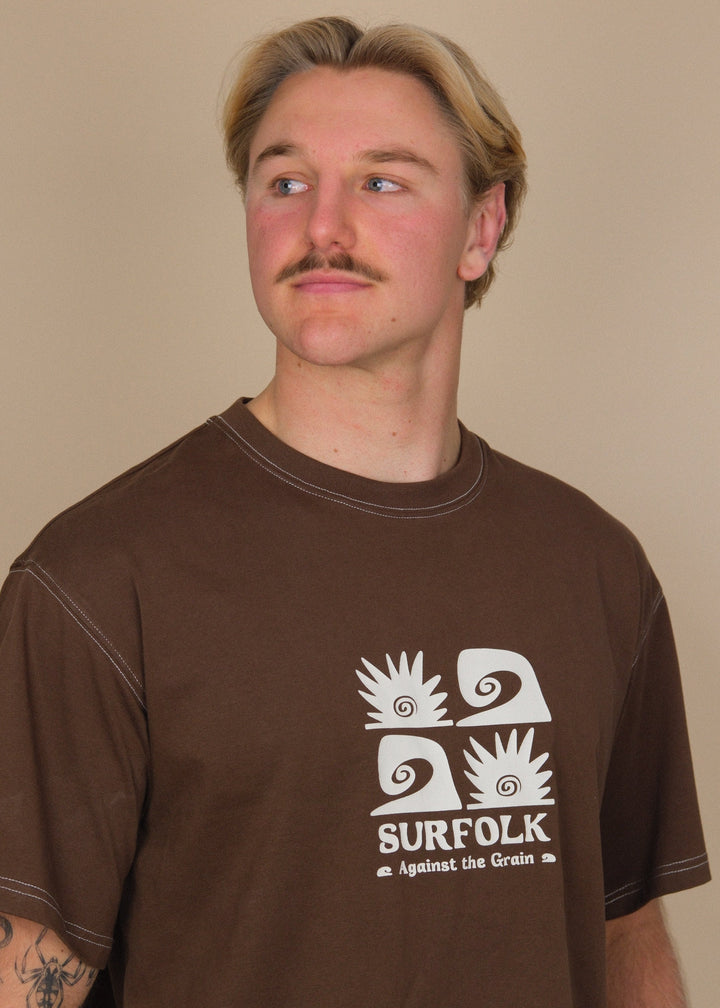 A man wearing a brown t-shirt with a white graphic print that reads &