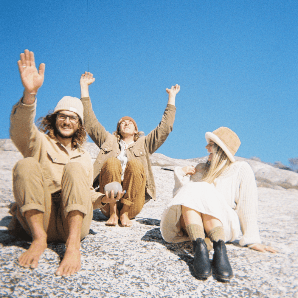 A 35mm film image of Three people sitting on a rocky surface with arms raised, enjoying a clear blue sky.