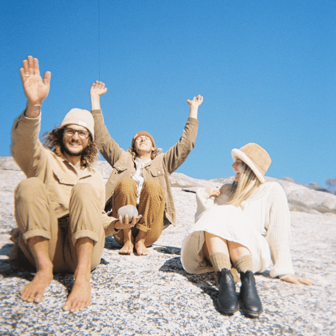 A 35mm film image of Three people sitting on a rocky surface with arms raised, enjoying a clear blue sky.