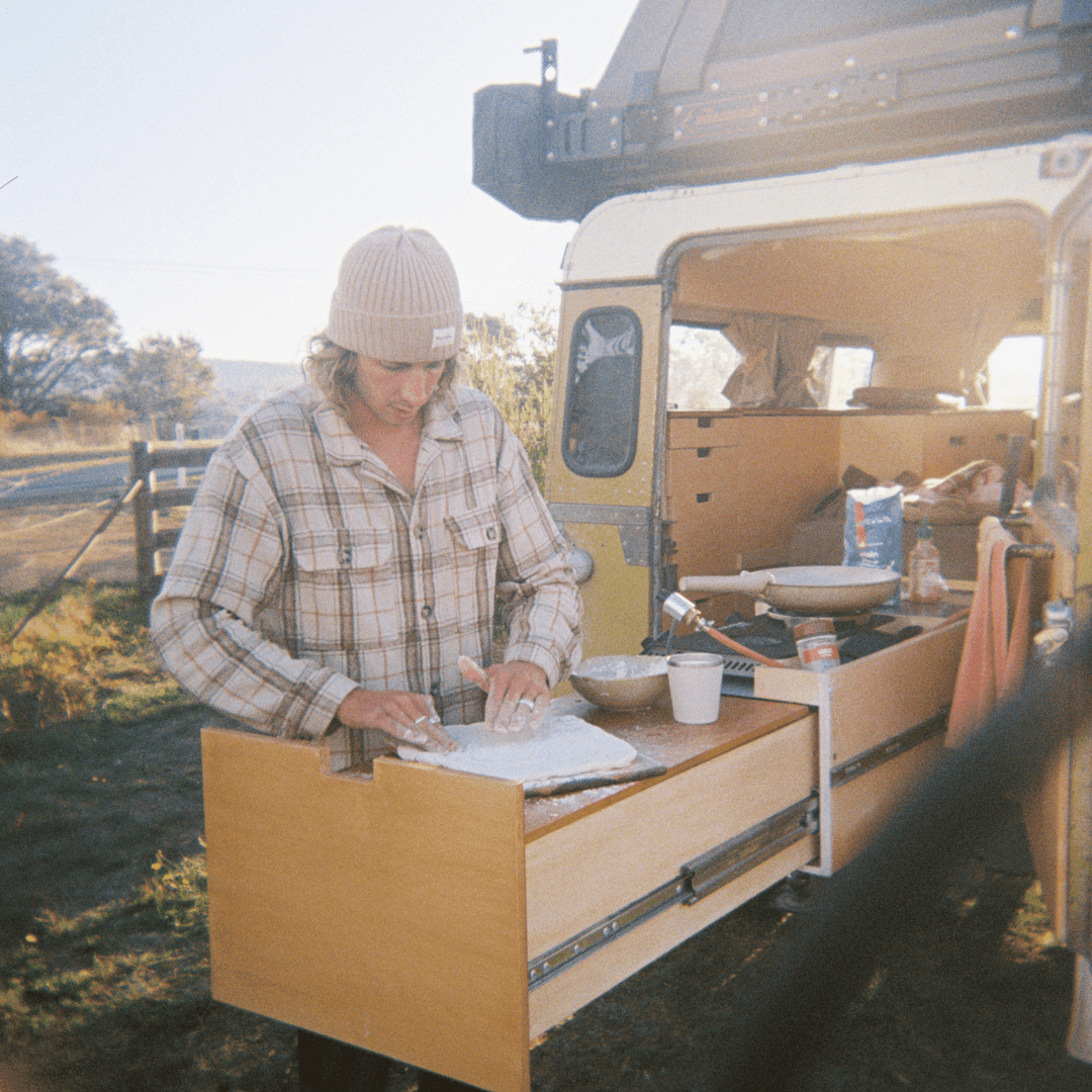 A 35mm film image of a man preparing food outdoors next to a van